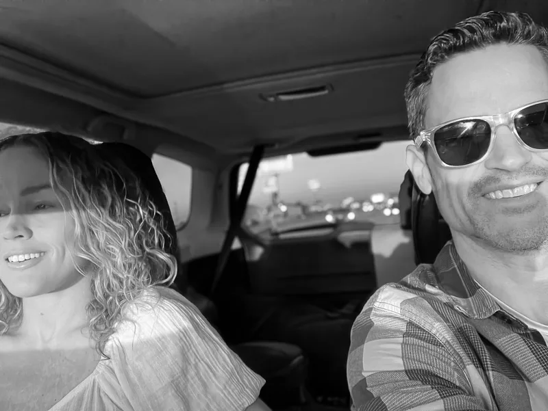 Man and woman sitting in car together, both smiling, black and white photograph