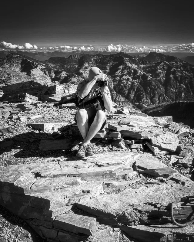 Man with camera photographing the mountain landscape from rocky summit, black and white photograph