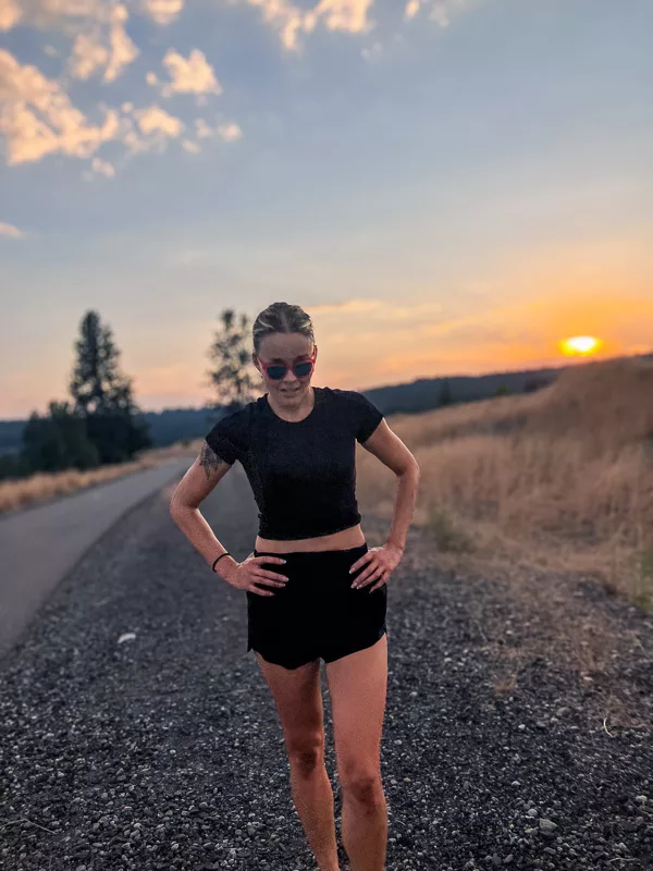 Woman in black athletic wear standing on rural road at sunset with golden light and open landscape