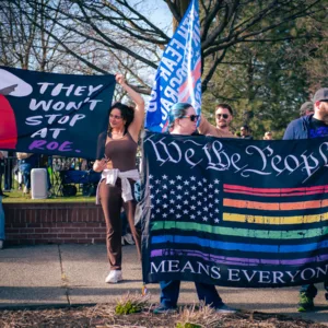 People holding large protest banners, including “We the People Means Everyone” and “They Won’t Stop at Roe”