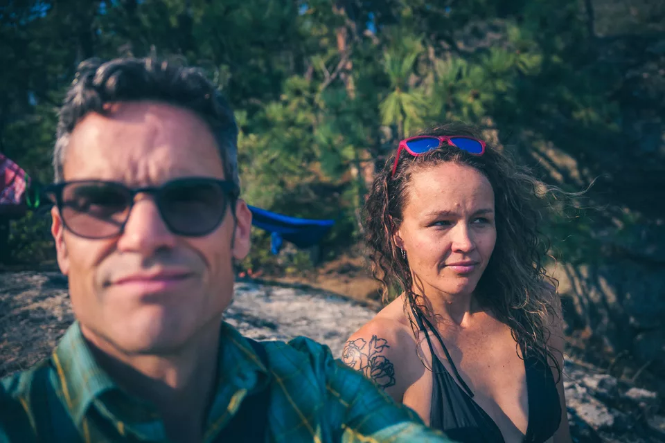 Lawrence Long and Erika Solberg sitting on sun-warmed granite among pines, a hammock strung behind them